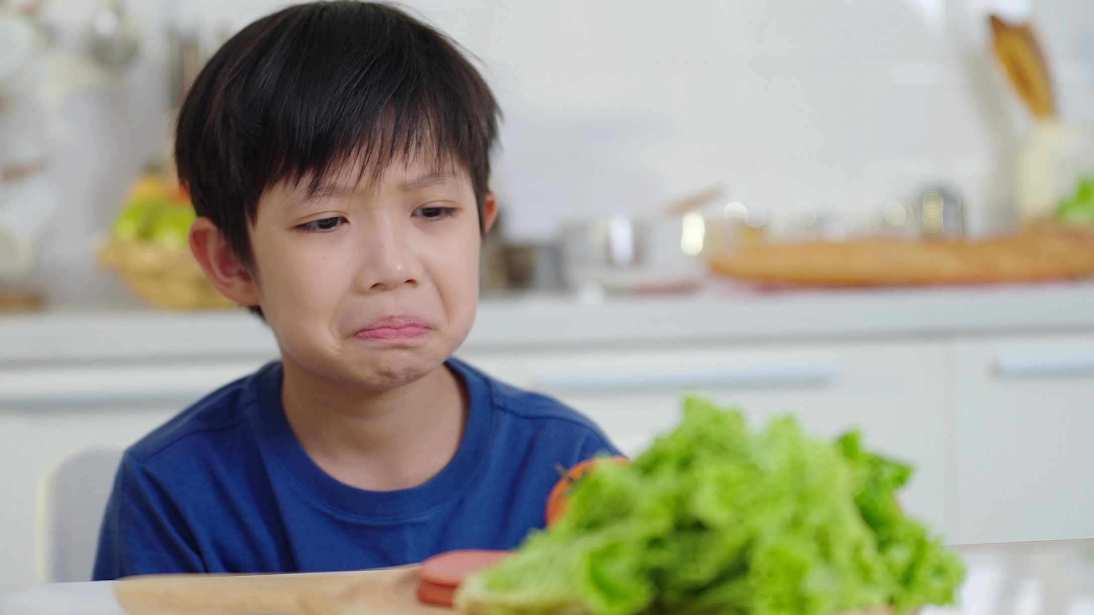 Children do not like to eat vegetables. Unhappy face of boy doesn't want to eat healthy vegetables