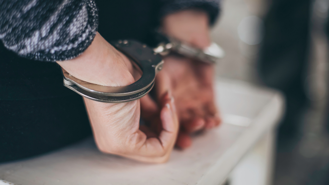 a woman sitting on a white bench with her hands in handcuffs
