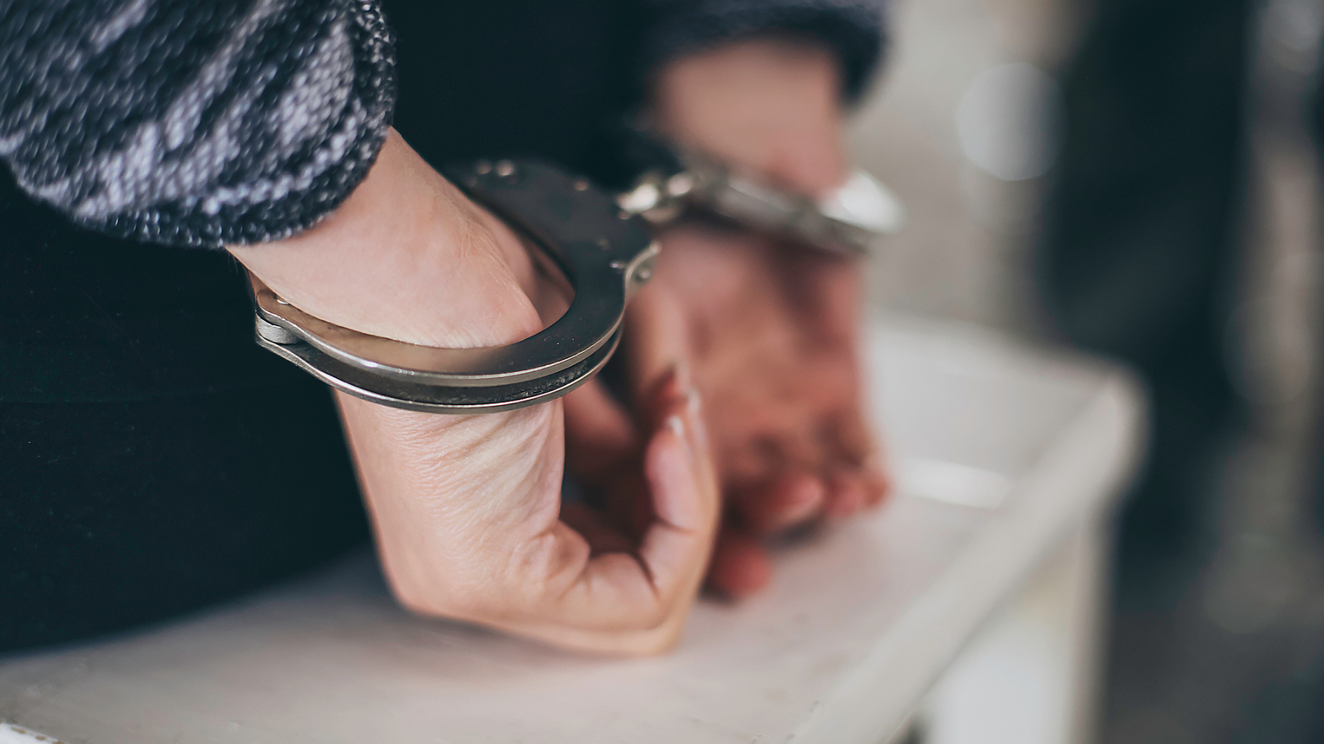 a woman sitting on a white bench with her hands in handcuffs