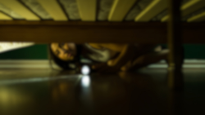 woman with a flashlight looking under a bed with wooden slats