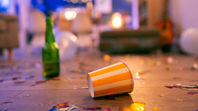 cup on floor with bottle in the background in messy house after party