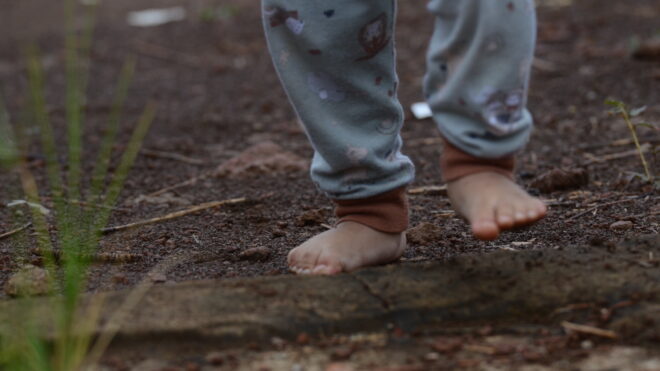 Barefoot baby girl walks on the ground to train her body sensors