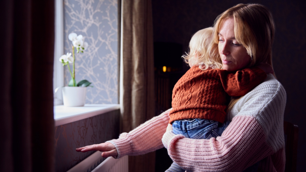 mom holding her baby in front of a window looking sad