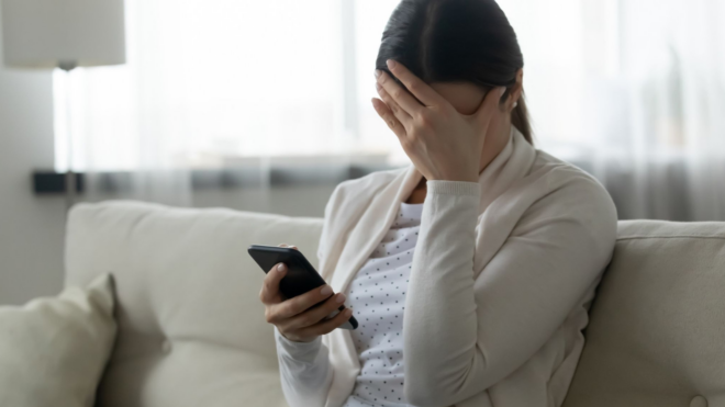 woman looking at phone with her hand over her face