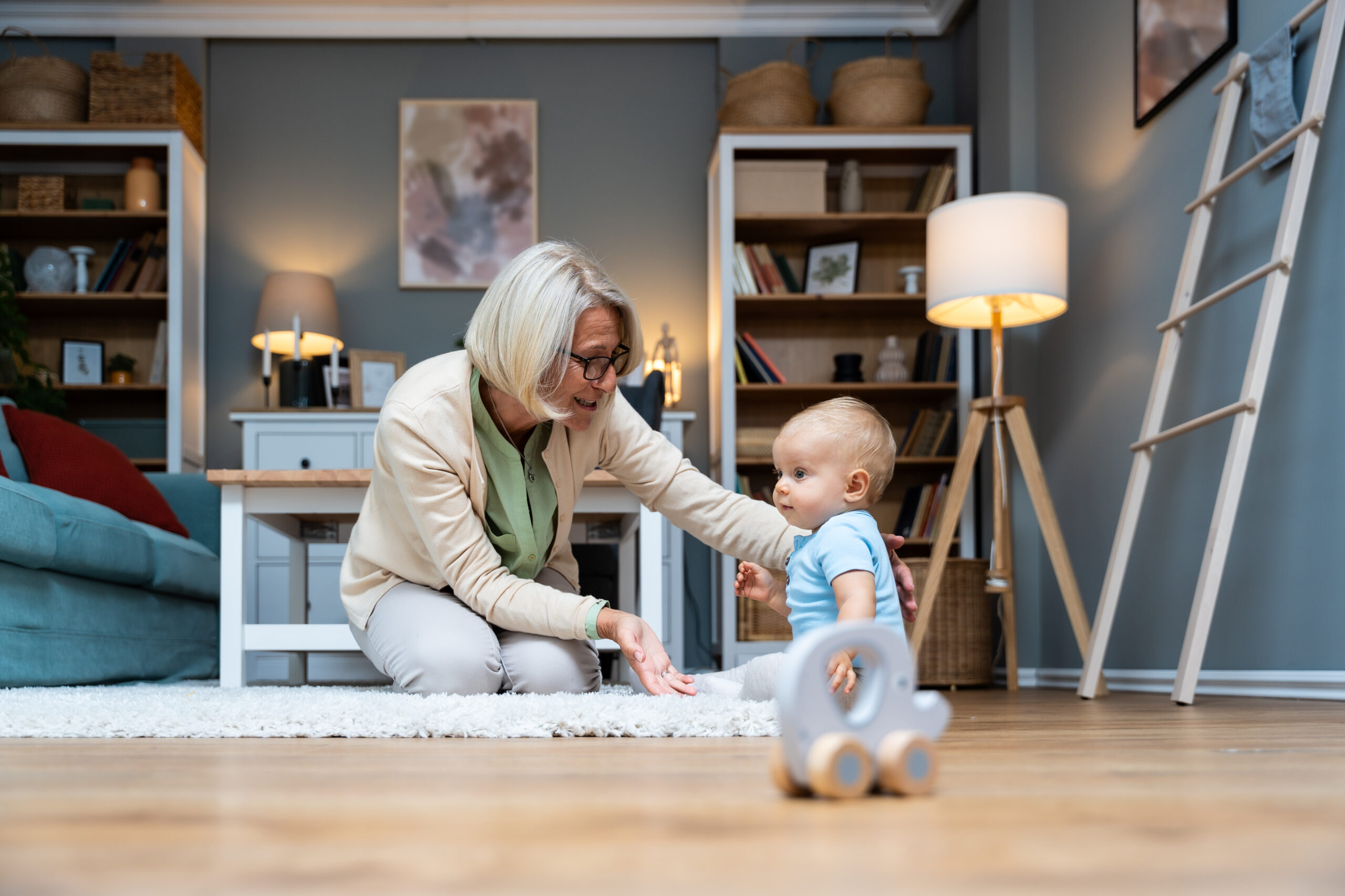 Grandmother taking care of her grandchild while his parents working. Senior woman work as a nanny, playing with young baby on the floor of the home. Grandson or granddaughter fun with his granny.