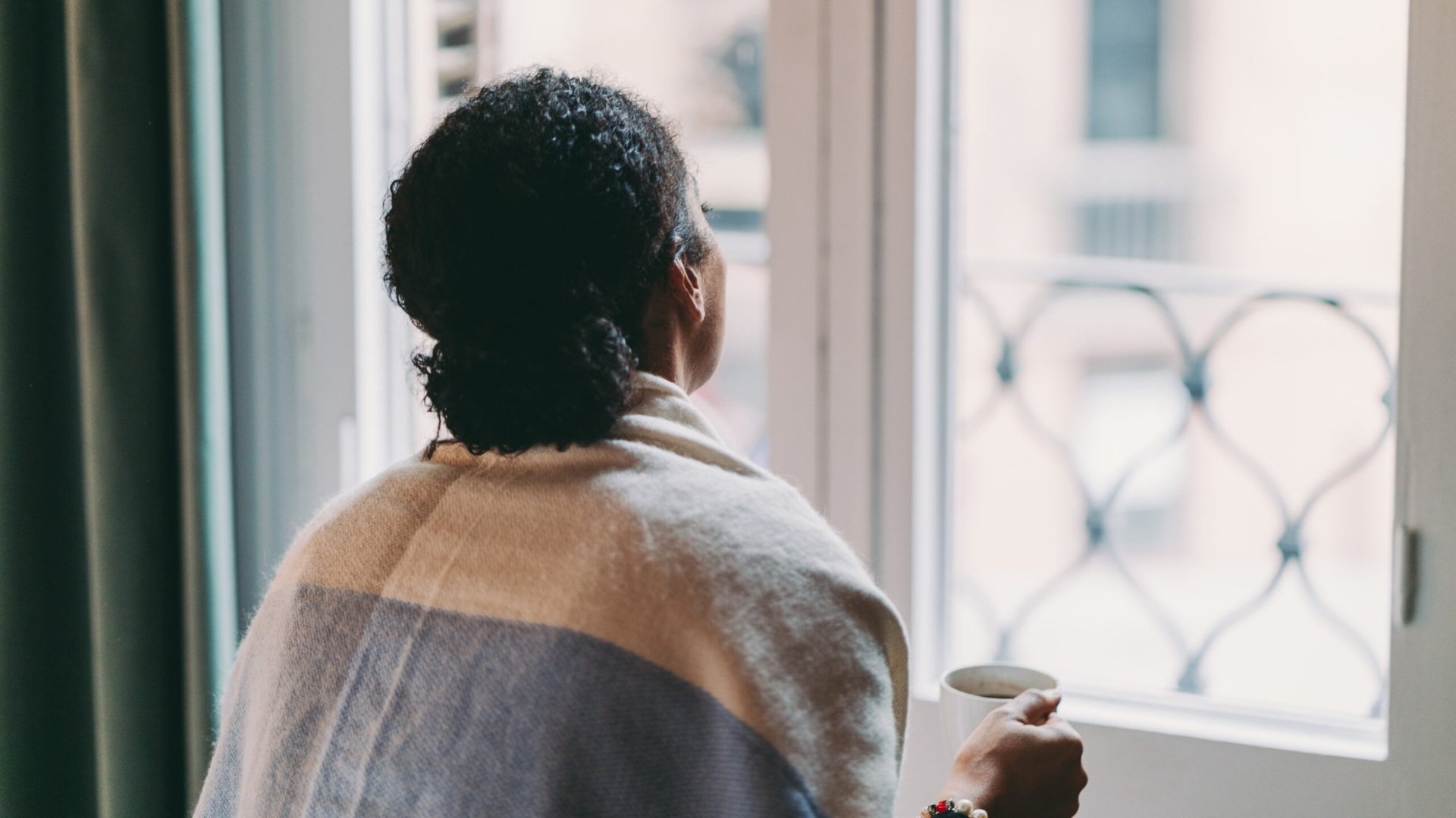 Black woman holding coffee mug and looking out the window