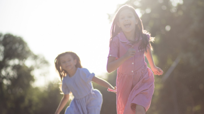 two young girls running outside in the sun