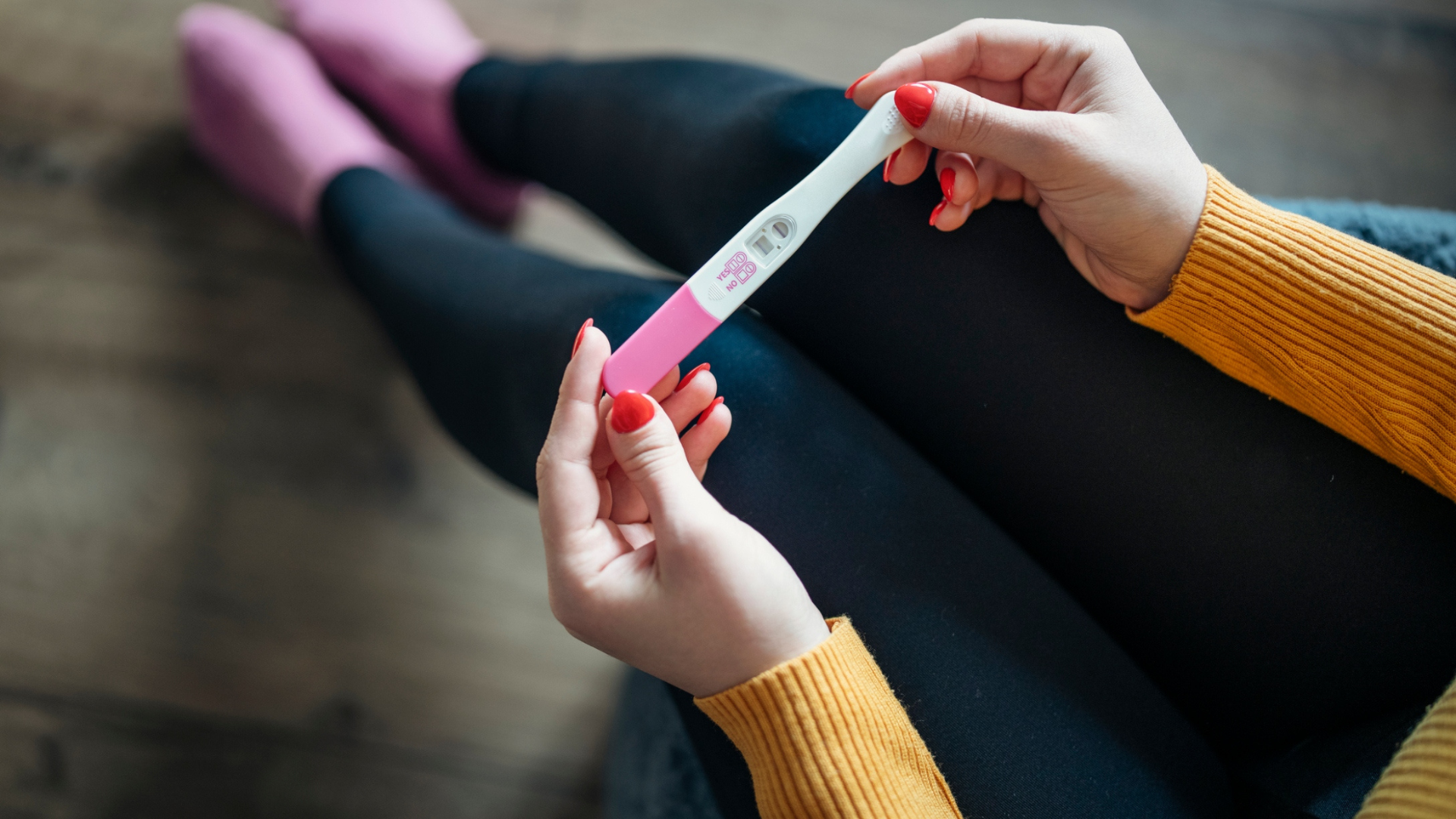 woman with painted nails holding a pregnancy test in her lap