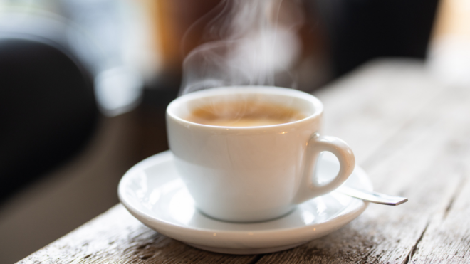 white coffee cup and saucer with steam on wooden coffee shop table