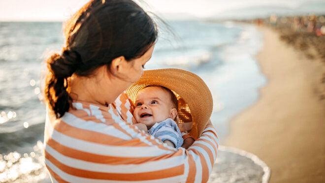 Mother holding baby near the sea, summer baby registry