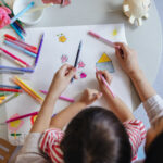 A From Above View Of An Unrecognizable Cute Asian Girl And Her Unrecognizable Nanny Drawing Using Markers