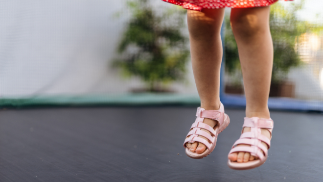legs of a little girl in a dress and sandals jumping on an enclosed trampoline