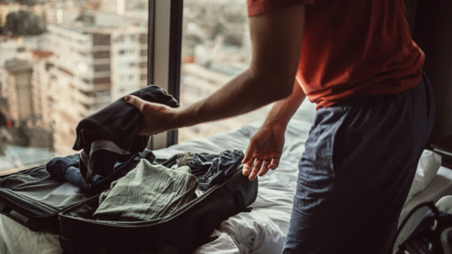 man in a hotel room packing a suitcase