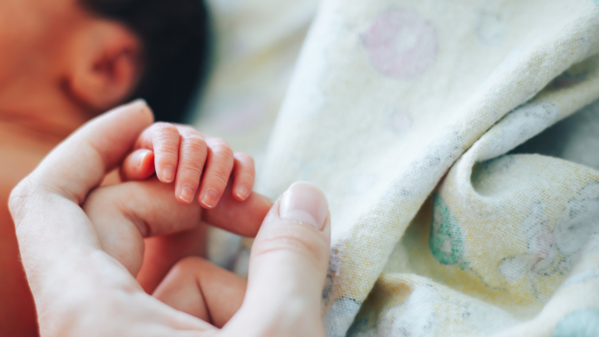 dark haired baby sleeping with mom holding onto its finger