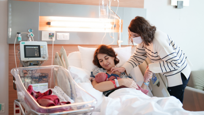 new mom cuddling her newborn while another woman looks over her shoulder