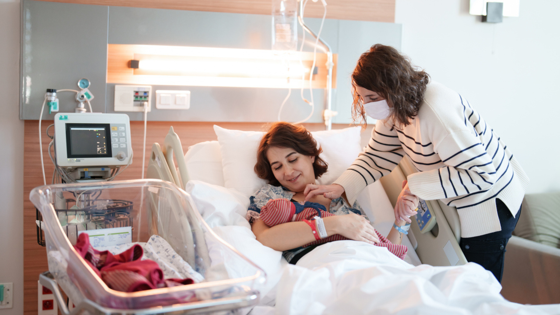 new mom cuddling her newborn while another woman looks over her shoulder