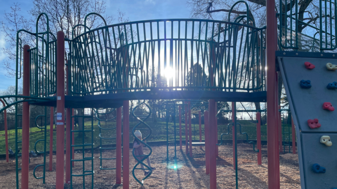 a bright sun shining behind empty playground equipment