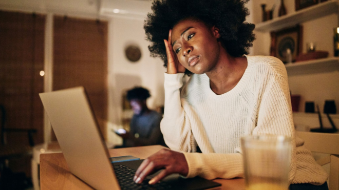 upset Black woman sitting in front of laptop with a man in the background