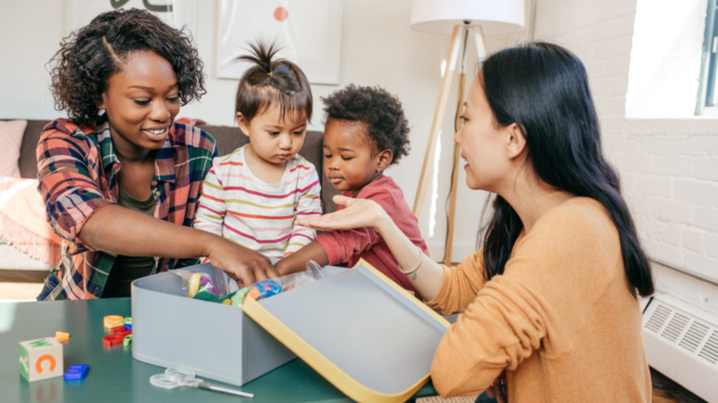Black mom and toddler looking through box of toys with Asian mom and toddler