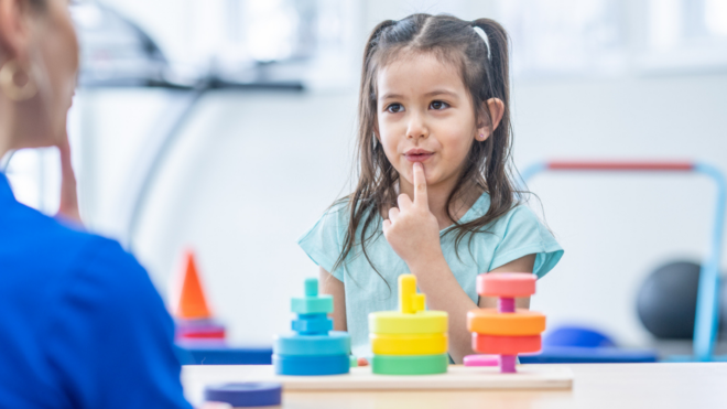 little girl with pigtails doing exercise with speech therapist