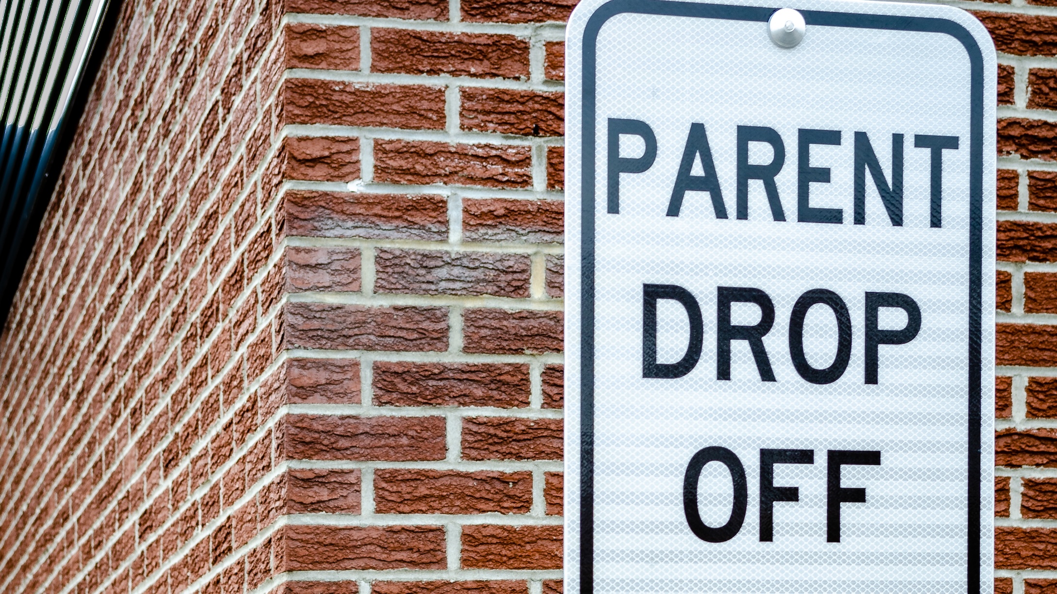 School Zone Parent Drop Off Sign next to a brown brick exterior wall