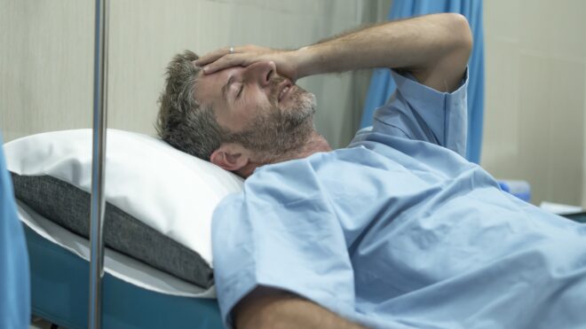 scared and worried man in pain at hospital room - attractive injured man lying on bed suffering painful problem feeling sick and stressed after suffering accident or serious disease