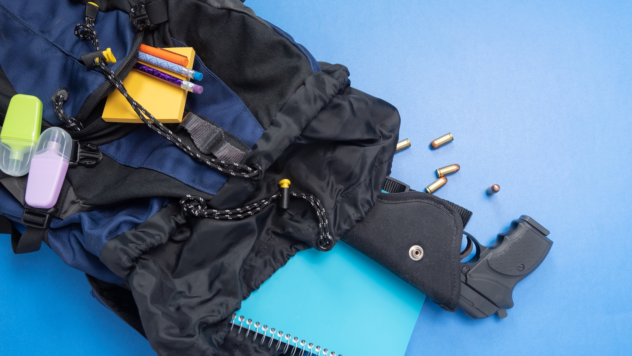 School accessories, blue and black backpack with a gun on a blue background. School violence concept.