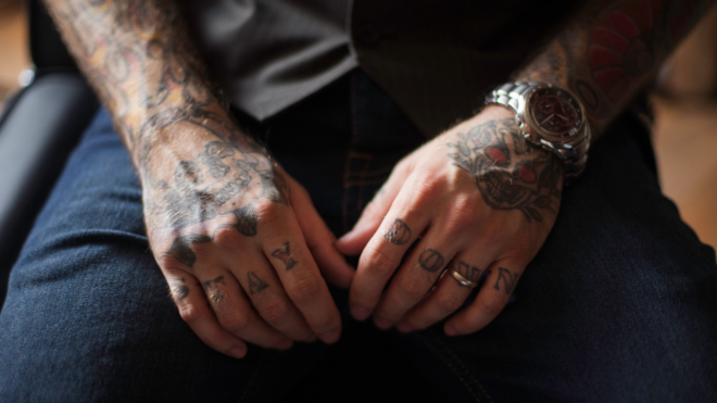 a man sitting in a chair showing his heavily tattooed arms and hands