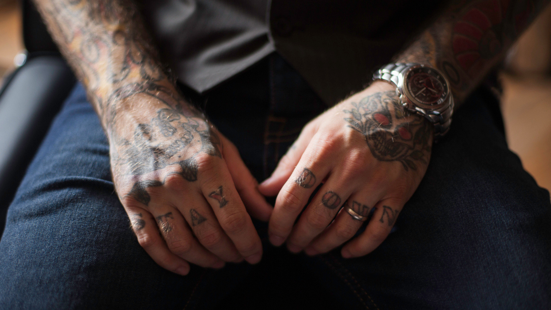 a man sitting in a chair showing his heavily tattooed arms and hands