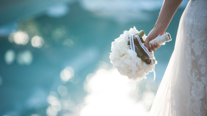 bride standing near a pool holding her bouquet