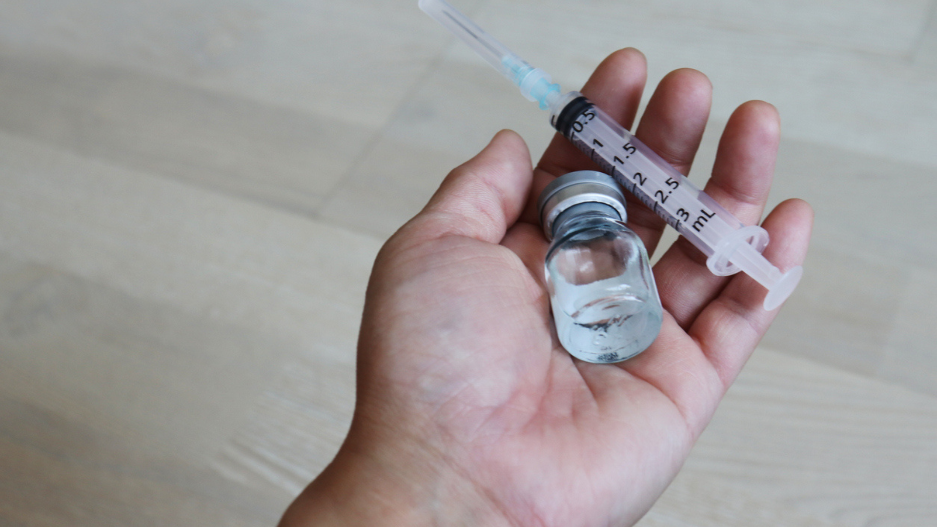 hand against a tan floor holding disposable syringe and medication