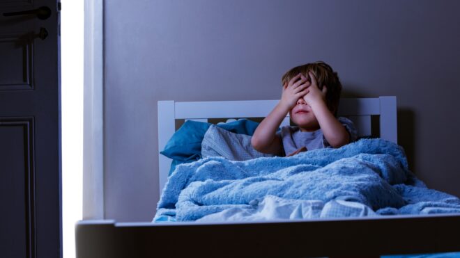 little boy in bed hiding under the covers from nightmare.