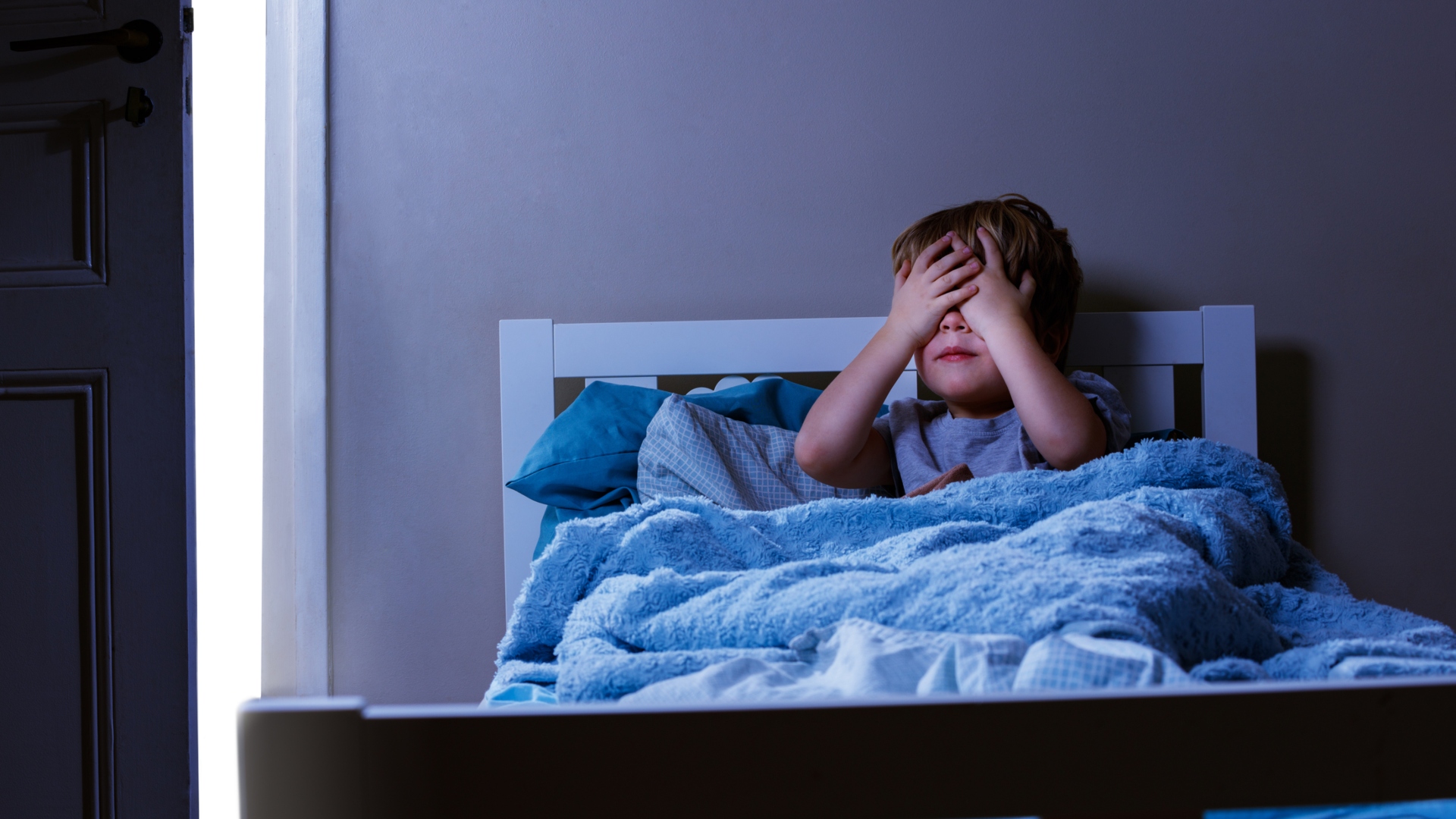 little boy in bed hiding under the covers from nightmare.