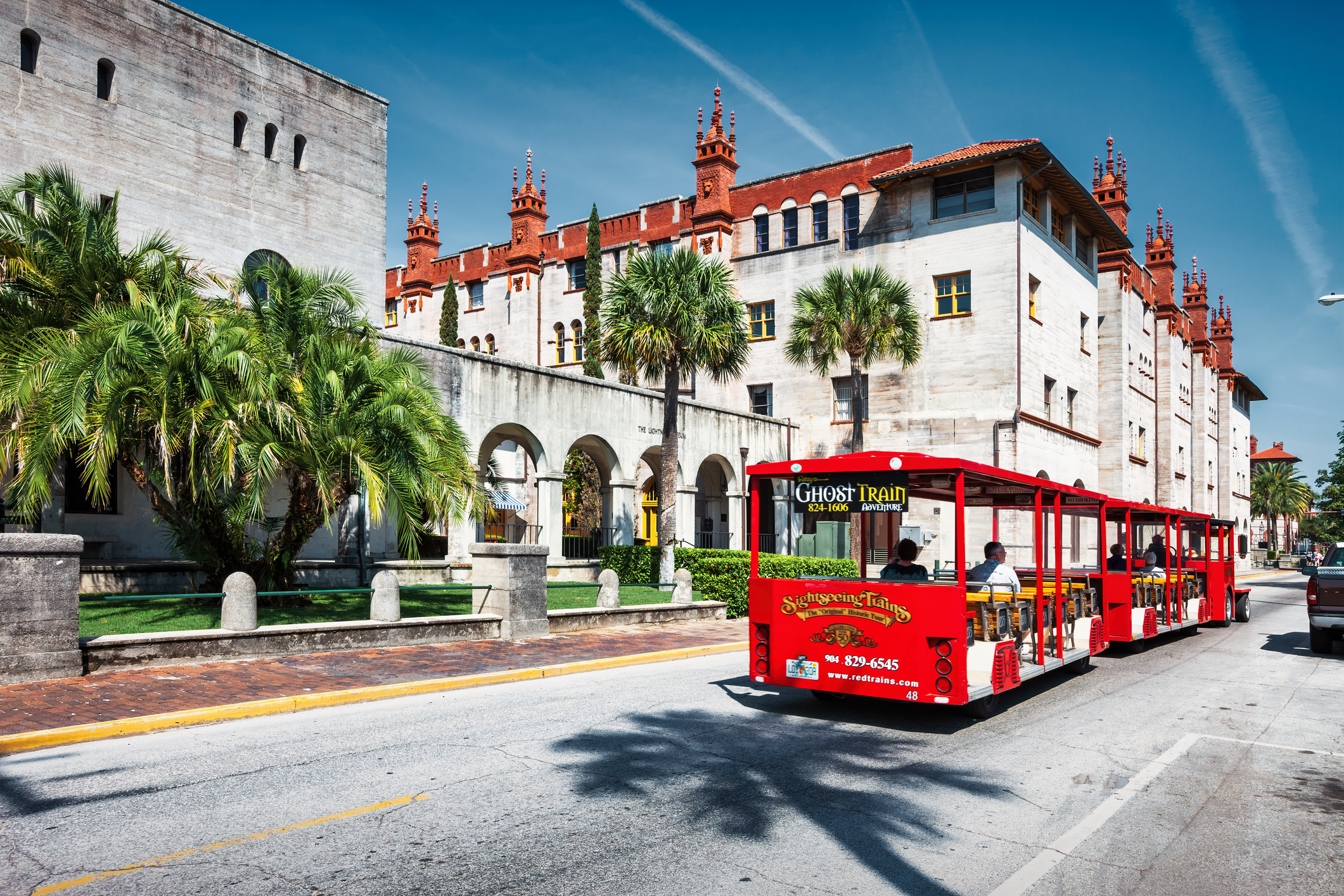 Sightseeing trolley with people moves past the Lightner Museum in downtown St. Augustine, Florida