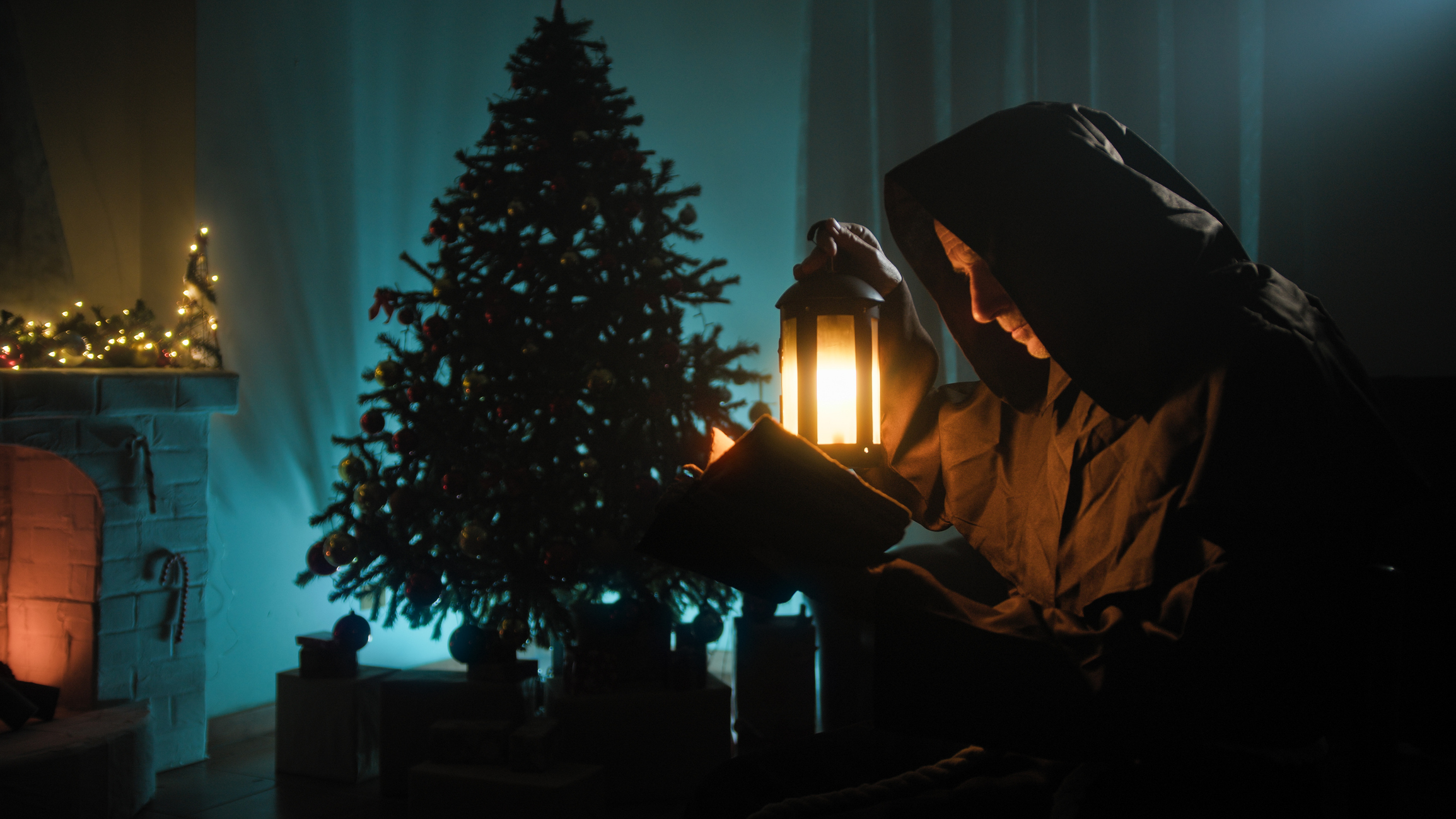 Mysterious Hooded Man reading book Mysterious Hooded Man Reads A Book Silhouette In Front Of Christmas Tree.