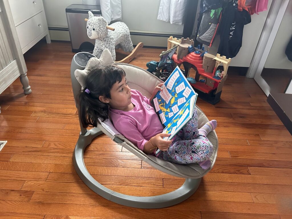 toddler in momcozy electric baby swing reading book