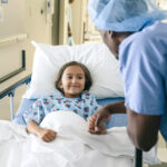 Doctor holding hand of girl in hospital bed