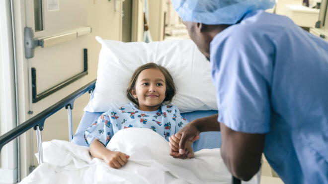Doctor holding hand of girl in hospital bed