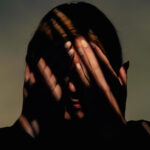 Woman covers her face with her hands. There are striped shadows on the face. Studio shot.