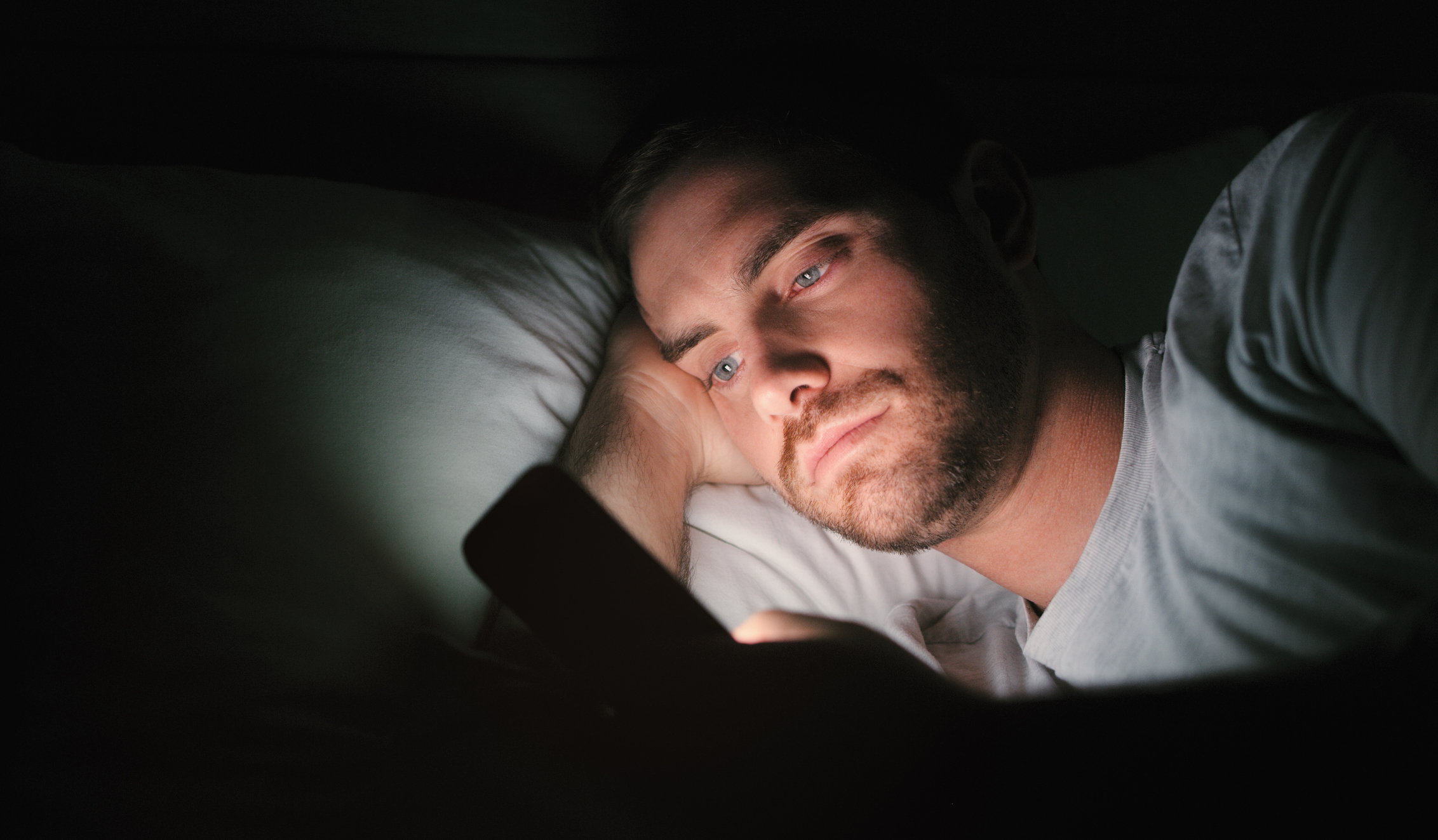 Shot of a young man lying in bed and using a smartphone at home