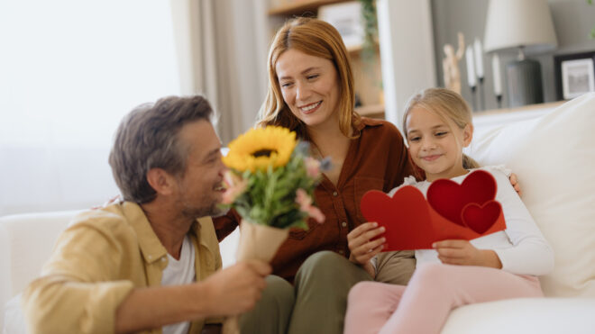 Happy family celebrating mother's day or valentine's day at home, daughter giving handmade greeting card and flowers to her mother
