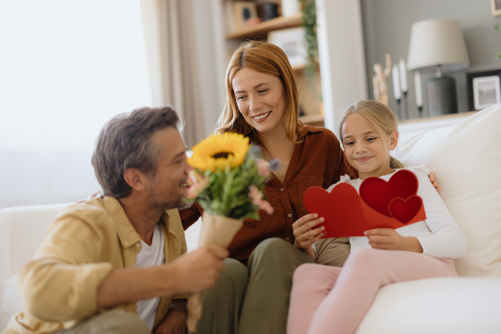 Happy family celebrating mother's day or valentine's day at home, daughter giving handmade greeting card and flowers to her mother