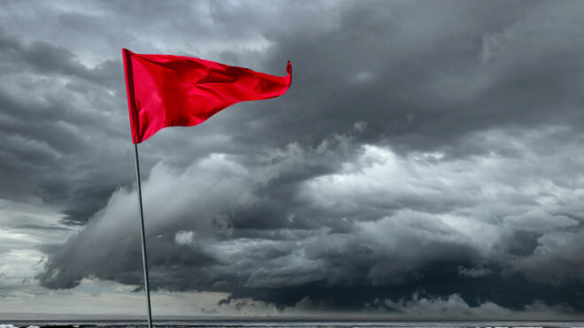 A red flag blows in the wind as it warns of an incoming storm in the distance.