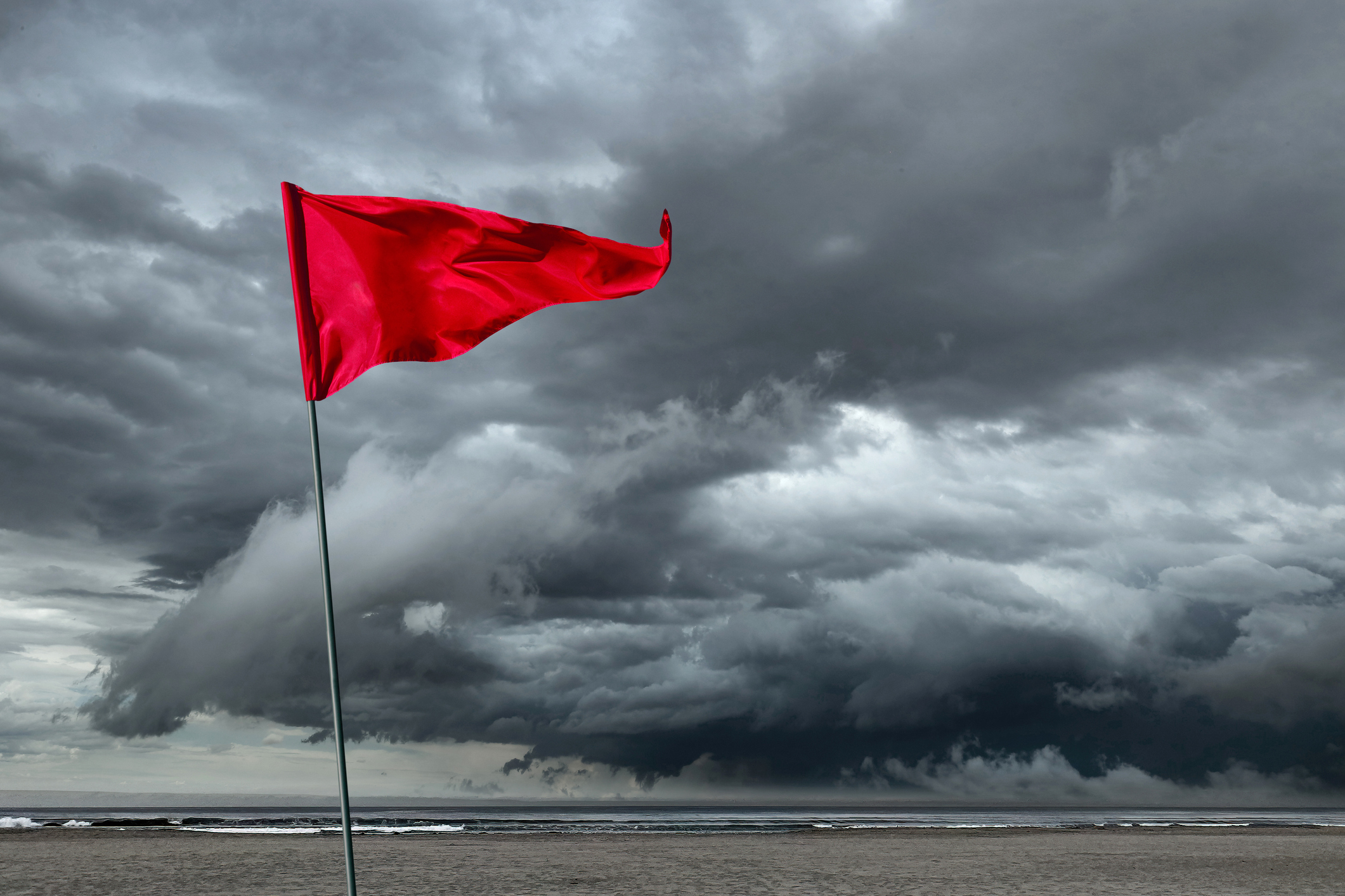 A red flag blows in the wind as it warns of an incoming storm in the distance.