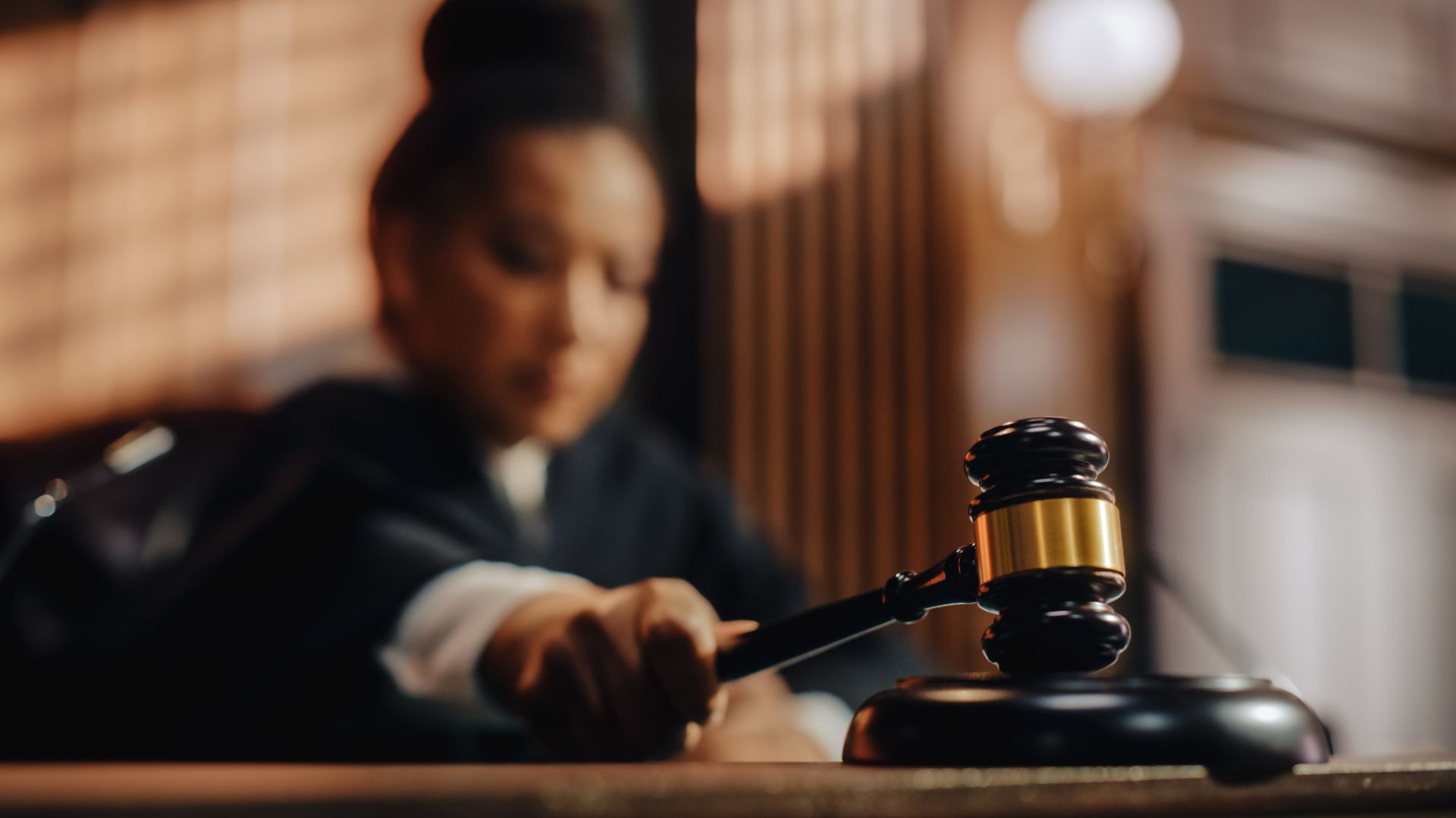 A blurred photo of a female judge sitting at her desk with her hand on her gavel