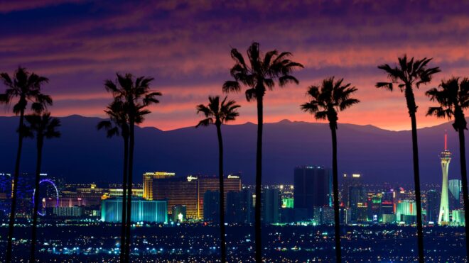 A moody photo of the Las Vegas cityscape with palm trees and pink clouds