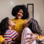 Mother and daughters embracing in the kitchen at home