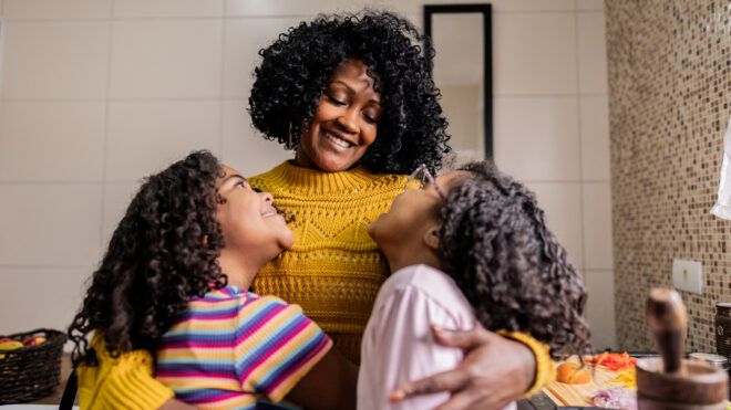 Mother and daughters embracing in the kitchen at home