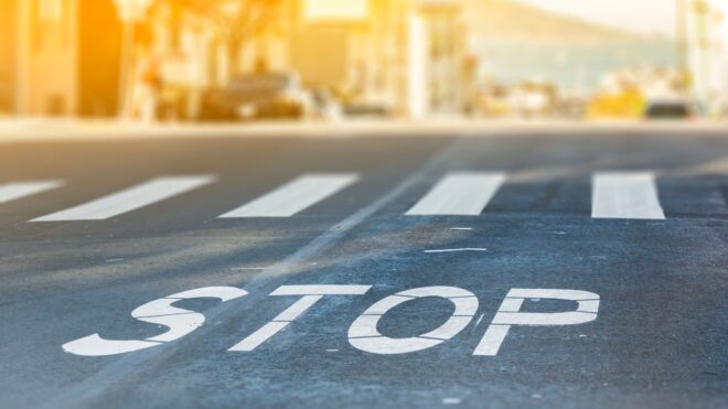 A close-up look at city crosswalk road with STOP written on the road and cars and a city landscape in the background
