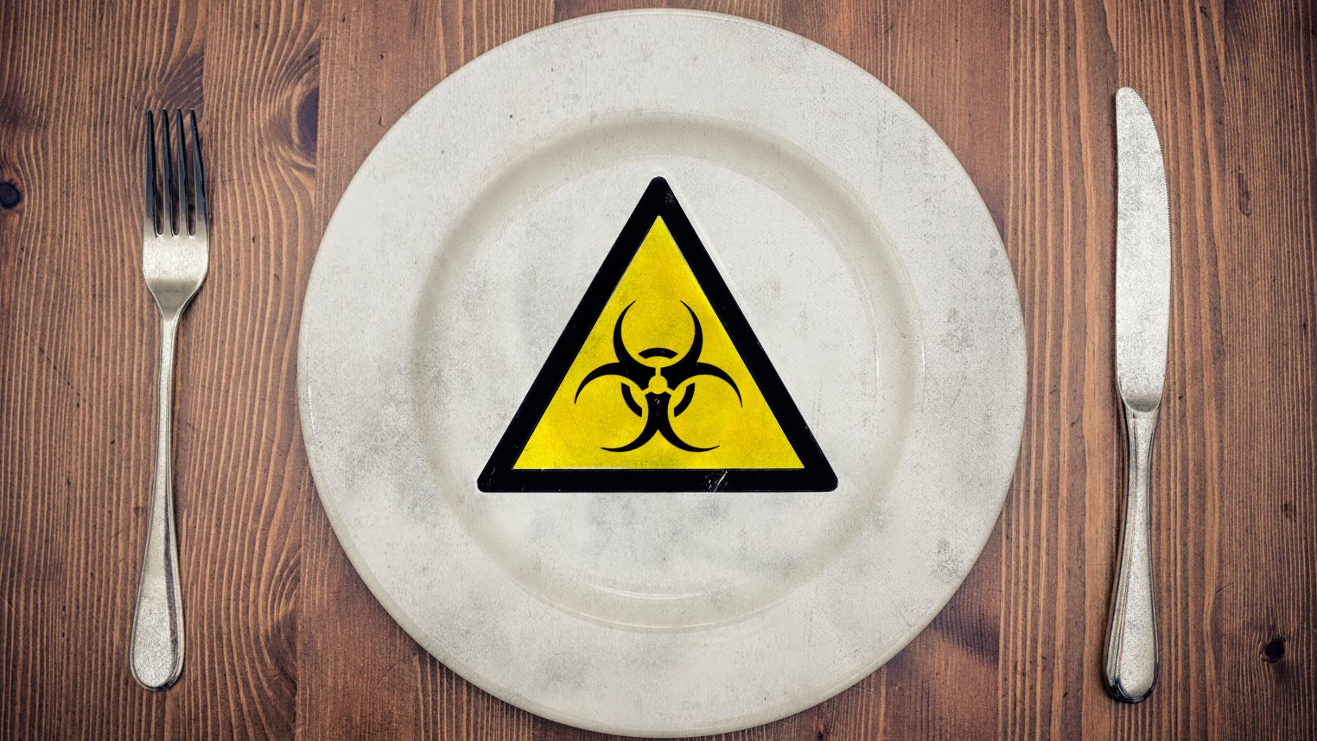 A photo of a white dinner plate with a fork and a knife on the side and a yellow poison warning in the middle of the plate